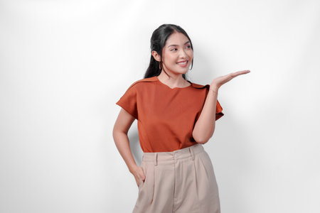 Beautiful young Asian woman in a brown shirt and taupe pants is presenting the copy space beside her, isolated by white background.の写真素材