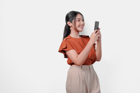 Happy young Asian woman is smiling while holding a cell phone to text someone or open social media, isolated by white background.の写真素材