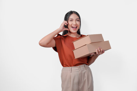 Cute young Asian woman is holding two boxes and making a finger heart shape gesture, isolated by white background.の写真素材