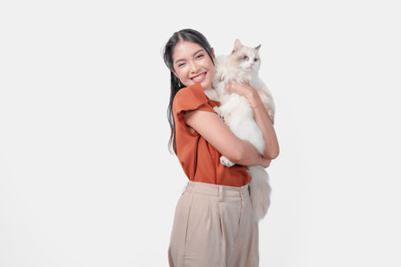 Cute young woman in brown shirt is holding a white ragdoll cat and hugging it over isolated white background.の写真素材