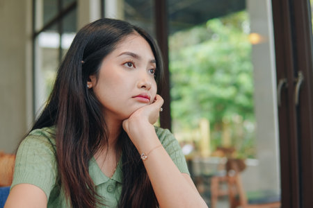 A woman is sitting at a table with her hands supporting chin, daydreaming looking front with deep in thought.の写真素材