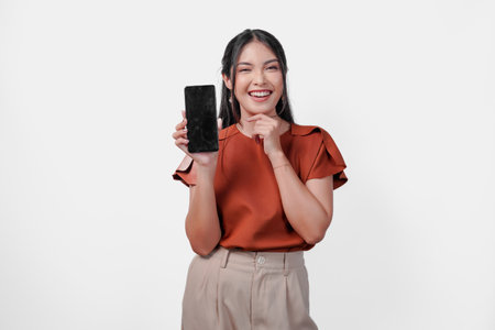 Beautiful young Asian woman in brown shirt smiling while showing the copy space on phone screen, isolated white background.の写真素材