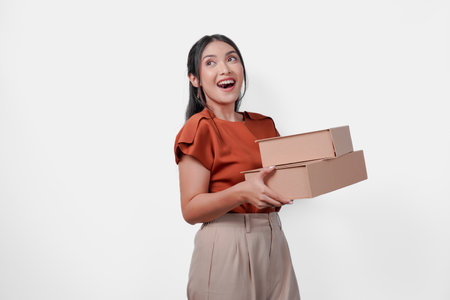 Happy young Asian woman is holding two boxes and smiling, looking to the copy space aside over isolated white background.の写真素材