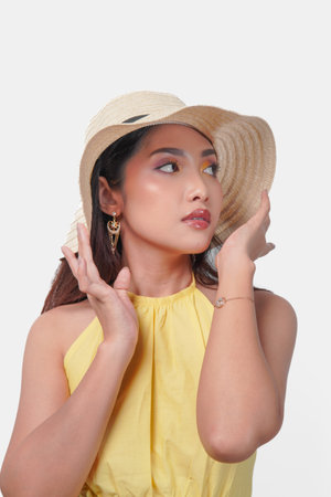 Beautiful young Asian woman in a yellow dress is wearing a straw hat striking a pose over isolated...