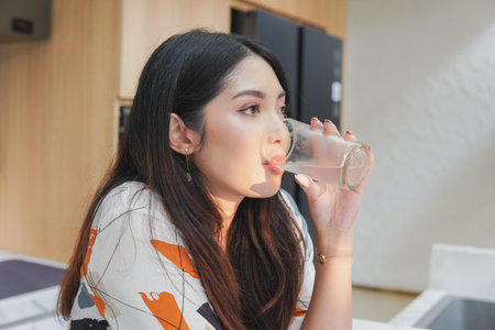Portrait of a young Asian woman is holding glass and drinking water in the villa kitchen.