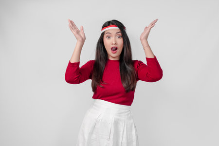 Shocked young woman in a red shirt and white pants is pointing to the copy space upwards, isolated white background.の写真素材