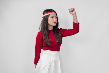Attractive young Asian woman in a red shirt and white pants is smiling and raising her hand in the air. Indonesia Independence Day concept.の写真素材