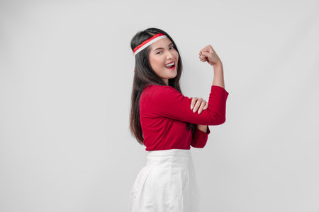 Confident young Asian woman in a red shirt and white pants is flexing strength by raising her arms and muscles.の写真素材