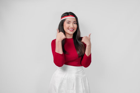 Excited young Indonesian woman in a red shirt and white skirt is giving a thumbs up gesture. Indonesia Independence Day concept.の写真素材