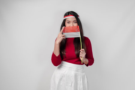 Young Asian woman holding a mini country flag, isolated by white background. Indonesia Independence Day concept.の写真素材