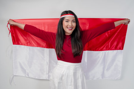 Excited young Asian woman is spreading Indonesian flag at her back and smiling. Indonesian Independence Day concept.の写真素材