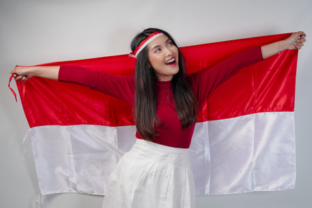 Excited young Asian woman is spreading Indonesian flag at her back and smiling. Indonesian Independence Day concept.の写真素材