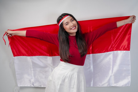 Excited young Asian woman is spreading Indonesian flag at her back and smiling. Indonesian Independence Day concept.の写真素材