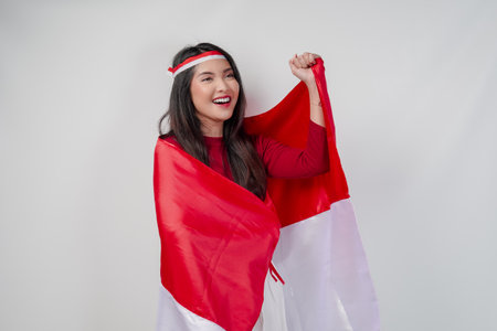Happy young Asian woman with Indonesia flag draped over her shoulders and raising fist hand gesture. Indonesia Independence Day concept.の写真素材