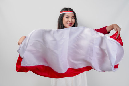Excited young Asian woman is spreading Indonesian flag and smiling proudly. Indonesian Independence Day concept.の写真素材