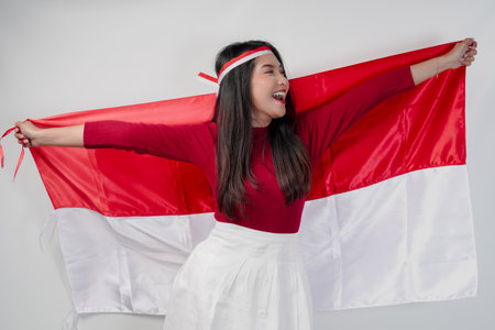 Excited young Asian woman is spreading Indonesian flag at her back and smiling. Indonesian Independence Day concept.の写真素材