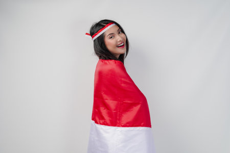 Smiling young Asian woman with Indonesian flag draped over her shoulders and she is posing for a picture. Indonesia Independence Day concept.の写真素材