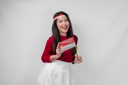 Smiling young Asian woman is holding mini country flag, isolated by white background. Indonesia Independence Day concept.の写真素材