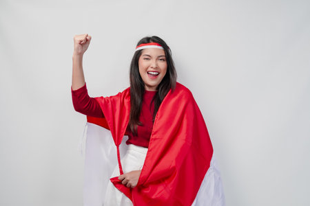 Happy young Asian woman with Indonesia flag draped over her shoulders and raising fist hand gesture. Indonesia Independence Day concept.の写真素材