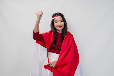 Happy young Asian woman with Indonesia flag draped over her shoulders and raising fist hand gesture. Indonesia Independence Day concept.の写真素材