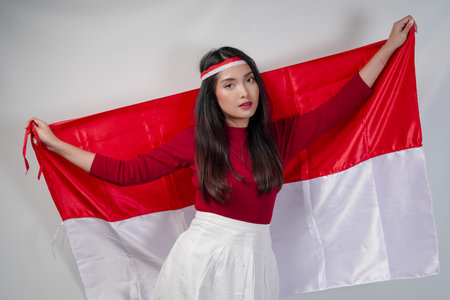 Elegant young Asian woman is spreading Indonesian flag at her back and posing like a model. Indonesian Independence Day concept.の写真素材