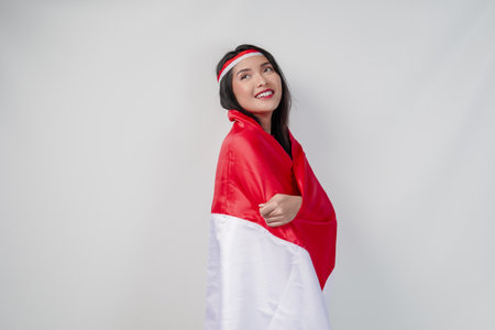 Smiling young Asian woman with Indonesian flag draped over her shoulders and she is posing for a picture. Indonesia Independence Day concept.の写真素材