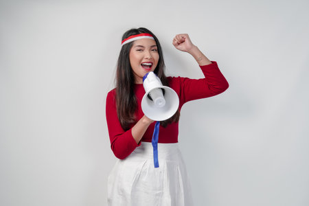 Attractive young Asian woman holding a megaphone and raise a clenched fist hand gesture. Indonesia Independence Day concept.の写真素材