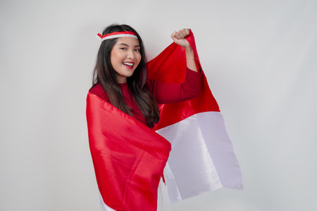 Happy young Asian woman with Indonesia flag draped over her shoulders and raising fist hand gesture. Indonesia Independence Day concept.の写真素材