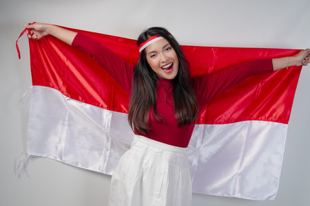 Excited young Asian woman is spreading Indonesian flag at her back and smiling. Indonesian Independence Day concept.の写真素材