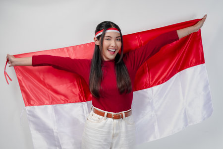 Joyful young Asian woman smiling and holding Indonesian flag behind. Indonesia Independence Day concept.の写真素材