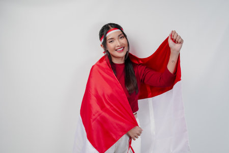 Confident Asian woman in a red and white outfit is covering herself with Indonesian flag and raising a fist. Indonesia Independence Day concept.の写真素材
