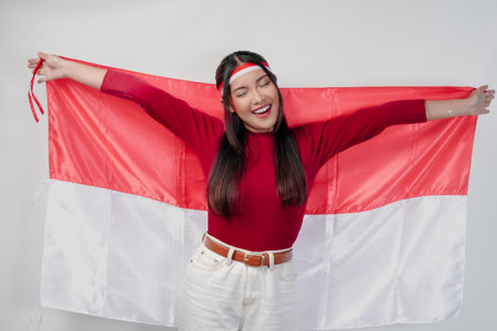 Joyful young Asian woman smiling and holding Indonesian flag behind. Indonesia Independence Day concept.の写真素材