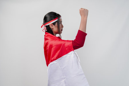 Side portrait of Asian woman covering herself with Indonesia flag and holding her fist up in the air. Indonesia Independence Day concept.の写真素材
