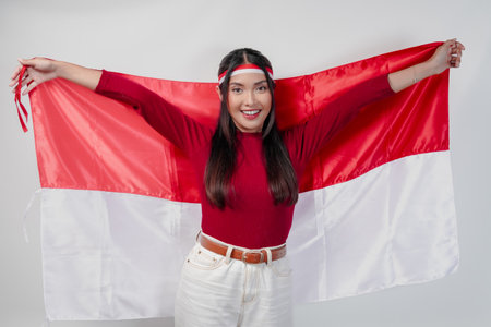 Joyful young Asian woman smiling and holding Indonesian flag behind. Indonesia Independence Day concept.の写真素材