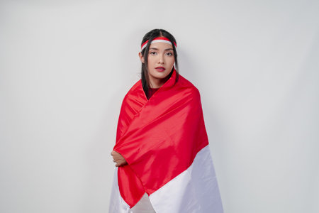 Smiling young Asian woman with Indonesian flag draped over her shoulders and she is posing for a picture. Indonesia Independence Day concept.の写真素材