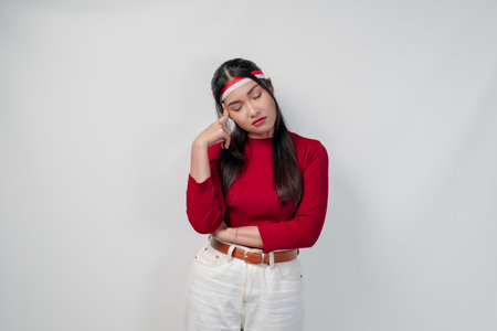 Thoughtful young Asian woman in a red shirt and white pants is confused and think of something.の写真素材