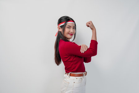 Confident young Asian woman in a red shirt and white pants is flexing strength by raising her arms and muscles.の写真素材
