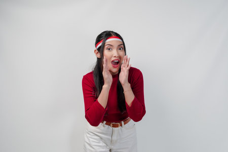 Cute young Asian woman in a red shirt and white pants is making gesture with hand, isolated by white background. Indonesia Independence Day concept.の写真素材