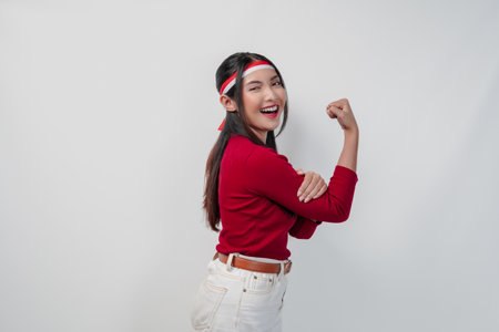 Confident young Asian woman in a red shirt and white pants is flexing strength by raising her arms and muscles.の写真素材