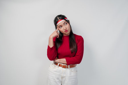 Thoughtful young Asian woman in a red shirt and white pants is confused and think of something.の写真素材