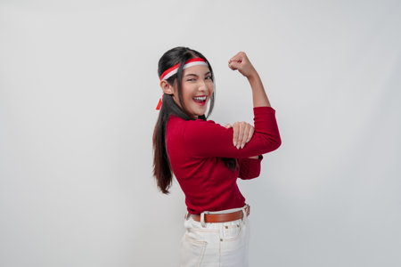 Confident young Asian woman in a red shirt and white pants is flexing strength by raising her arms and muscles. Indonesia Independence Day concept.の写真素材