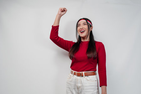 Cheerful young Asian woman in a red shirt and white pants is smiling and raising her hand in the air. Indonesia Independence Day concept.の写真素材
