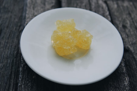 Crystal rock sugar on top of a white plate placed on a wooden table, usually used at a traditional...