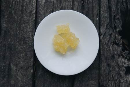 Crystal rock sugar on top of a white plate placed on a wooden table, usually used at a traditional...
