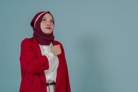Young Indonesian woman in a red jacket and hijab doing proud and brave salute gesture while looking up. Indonesia Independence Day concept.の写真素材