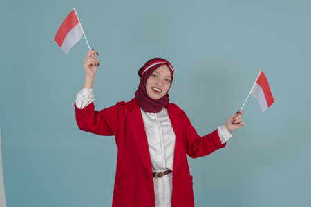 Happy Indonesian woman wearing a red jacket and hijab holding two mini country flags. Indonesian Independence Day concept.の写真素材