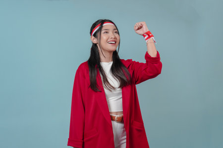 Joyful young Asian woman in a red jacket is raising her hands in the air with happy successful expression. Indonesia Independence Day concept.の写真素材