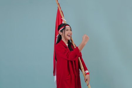 Indonesian woman wearing a red jacket holding a flag while raising fist gesture with excited...