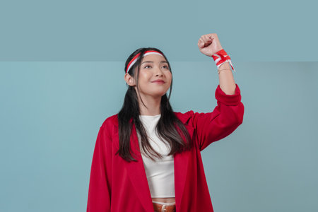 Joyful young Asian woman in a red jacket is raising her hands in the air with happy successful expression. Indonesia Independence Day concept.の写真素材