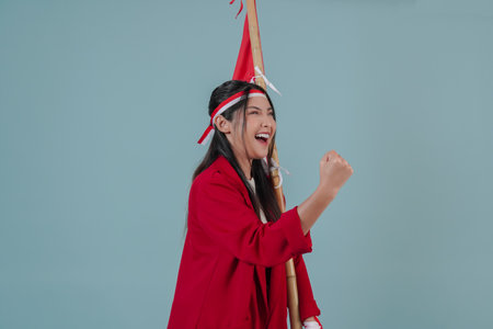 Close up portrait of Indonesian woman wearing a red jacket holding a flag while raising fist gesture. Indonesian Independence Day concept.の写真素材